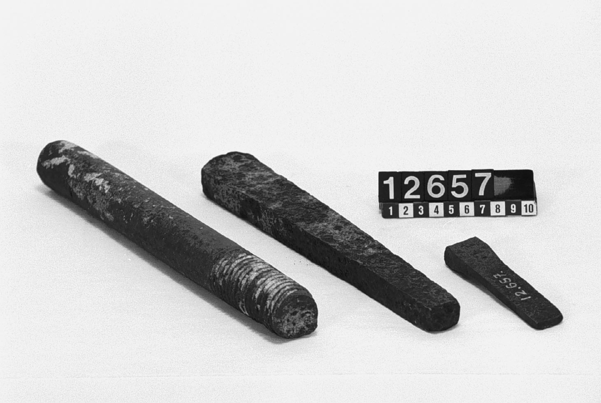 Tre föremål av järn. Stycke av rund stång gängad i ena ändan, längd: 295 mm, diameter: 34 mm. Två kilformade föremål, längd: 260 mm resp. 105 mm.