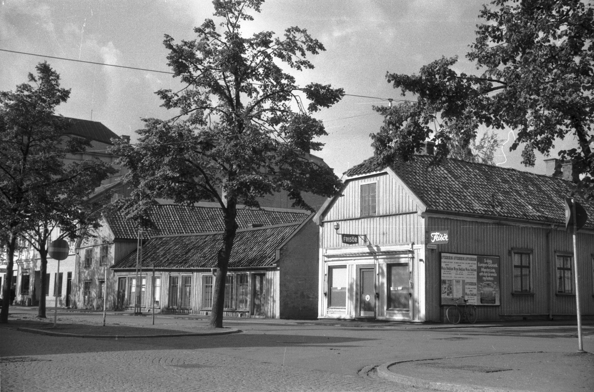 Trähus med en Frisörsalong i hörnet Kanalgatan - Björngränd i Jönköping. En cykel står lutad mot en skylt för affischering, som bland annat gör reklam för bilmärket Wolksvagen.