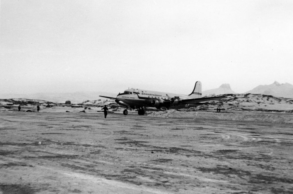 Lufthavn/Flyplass. Bodø. Et fly, DC-4, fra SAS har nettop landet og parkert på tarmac/flyoppstillingsplass. I bakgrunnen øya Landegode.