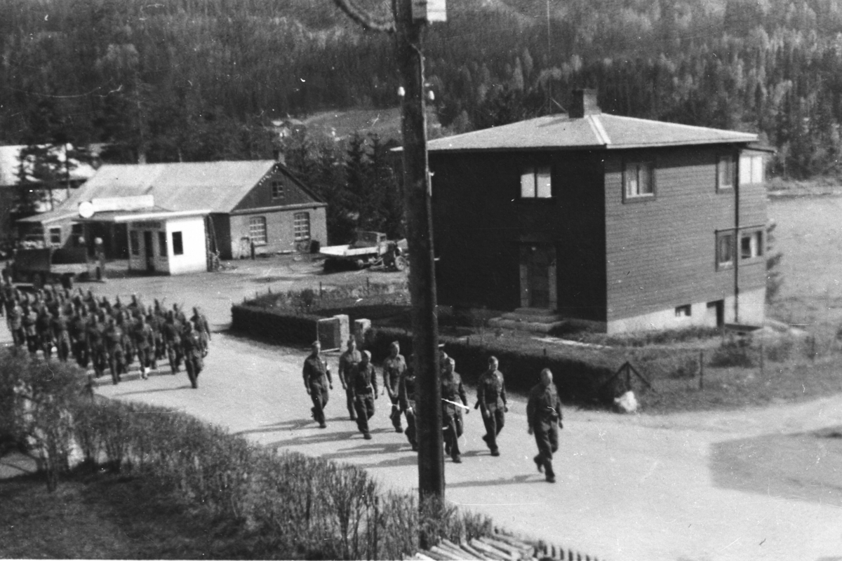 Mønstring av heimevernsstyrkane 17. mai 1945. Gol sentrum: Sentrumsvegen ved Fjordgløtt (gnr 9/brnr 55). Viko Auto i bakgrunnen.