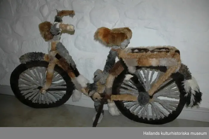 Cykel med damram klädd med syntetpäls i bruna, grå och vita nyanser. Hela cykeln är täckt med päls, även styre, däck, trampor och ekrar.
