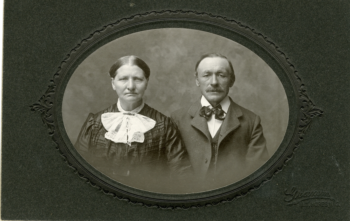 Portrett av en eldre kvinne og mann. Kvinnen er iført en kjole med stor krage mens mannen er iført dress med sløyfe i halsen.