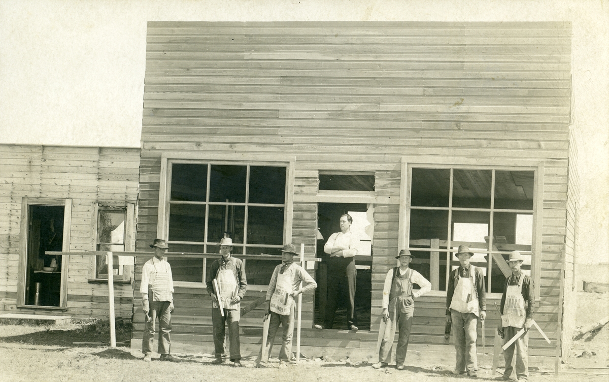 Bildet viser 6 karer i arbeidsklær foran et hus under oppføring.