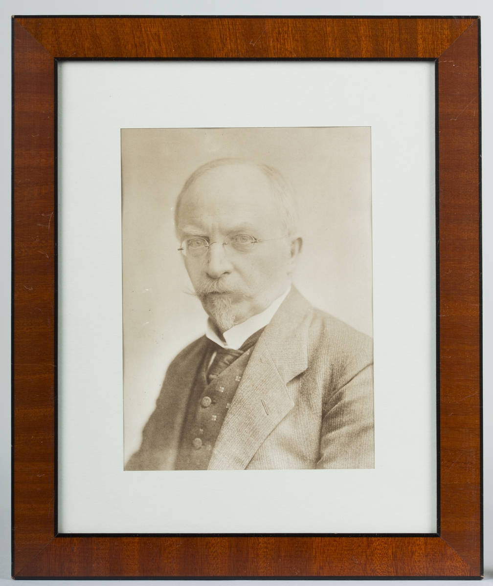 Svart- hvitt fotografisk portrett av en mann satt i glass og ramme.