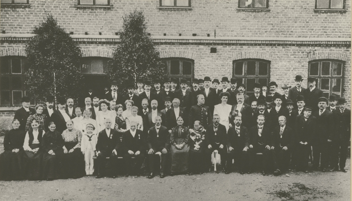 Gruppbild utanför stora sliperiet vid Orrefors glasbruk år 1909 med de nio medaljörerna, bolagsstyrelsen med flera.