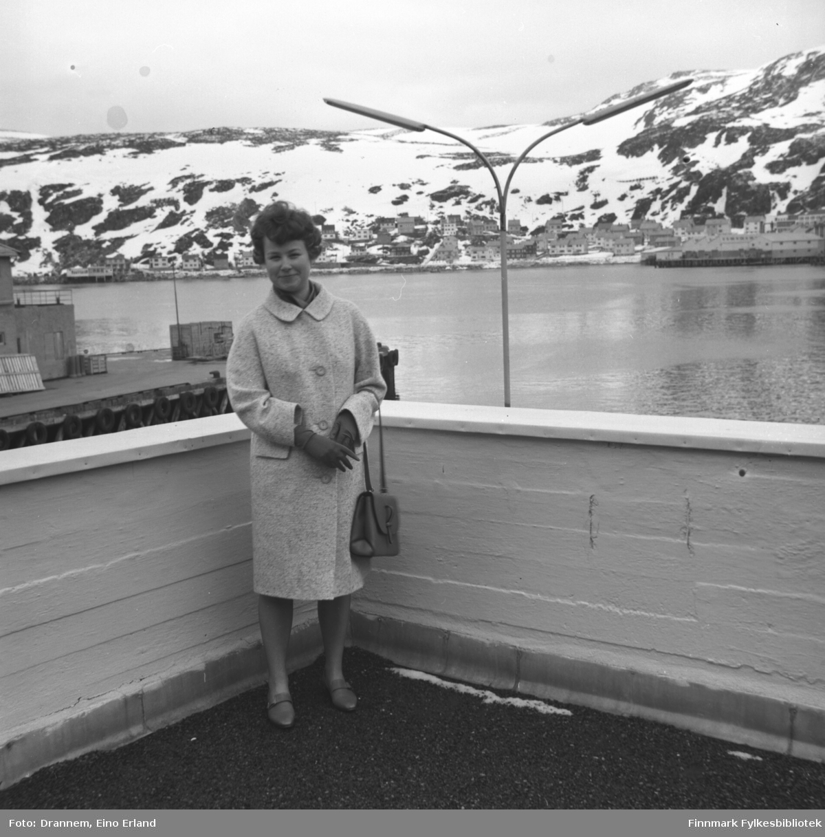 Turid Karikoski står på verandataket til Tollboden i Hammerfest. Bydelen Molla ses i bakgrunnen.