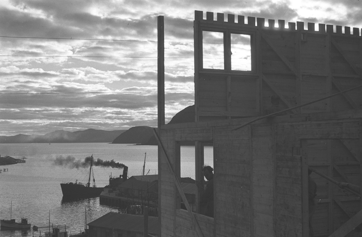 Gjenreisning. Et hus settes opp i Honningsvåg. I bakgrunnen et fraktskip ved kaia. 1946/47.
