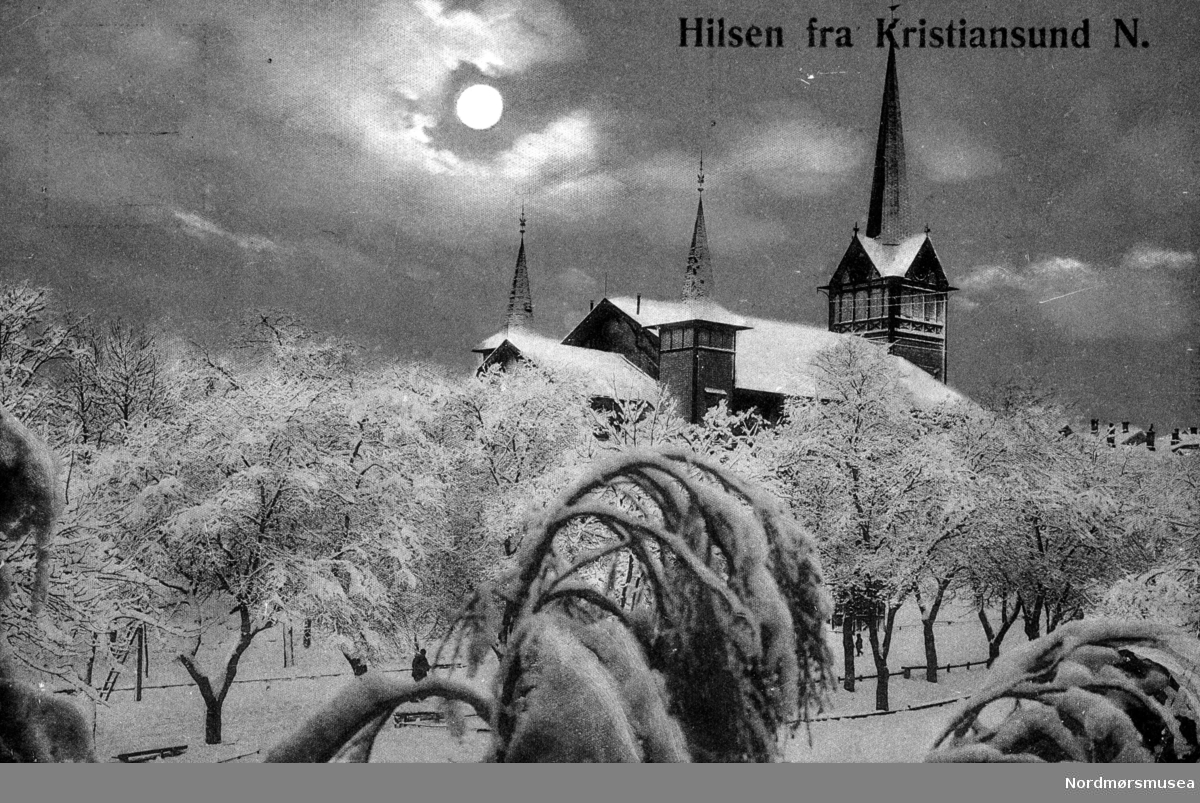 ";Hilsen fra Kristiansund N."; En vinterdag på Kirkelandet i Kristiansund, hvor vi ser fra den snøkledte parken i front, samt gamle Kirkelandet kirke i bakgrunnen. Fra Nordmøre museums fotosamlinger.  /Reg:EFR2013/
