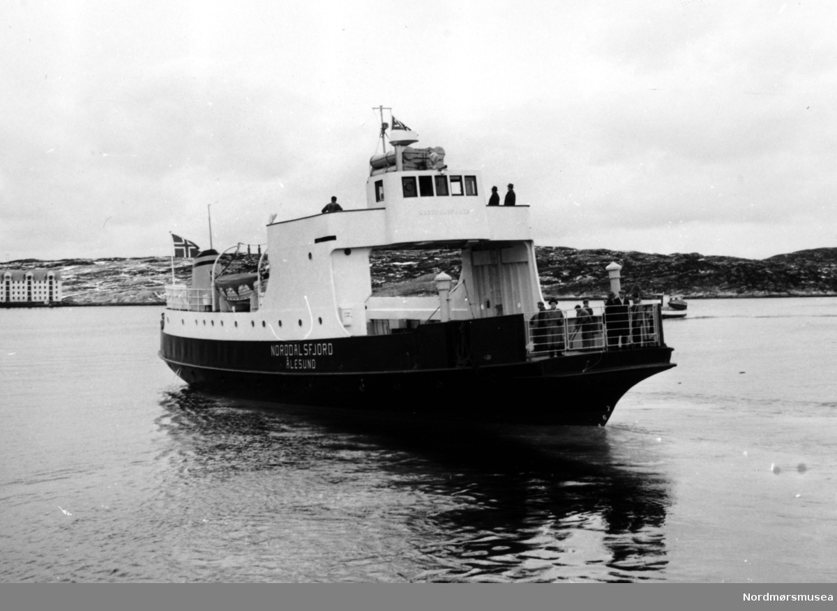 Bildet viser Storviks Mek. Verksteds nybygg B/F"Norddalsfjord" bnr.14 som legger ut fra piren på teknisk prøvetur. Verkstedflagget og det norske flagget er oppe.

"Norddalsfjord" ble levert til Møre og Romsdal Fylkesbåtar 15. mars 1961 og hadde følgende hoveddimensjoner: L 31,20 m x B 8,55 m x D 3,35 m og hadde en tonnasje på 159 bruttoregistertonn. Fremdriftsmaskineriet består av 3 Volvo Penta turboladede dieselmotorer type TMD96 på til sammen 420 hk som via kilremdrift var koblet til et felles gir og propellaksel med vribar propell, slik at hver enkelt av motorene kunne kjøres separat. Fergen hadde 2 Bolinders vekselstrømsaggregater type 1052MG på 23 hk hver tilkoblet en generator på 17 kW. Fergen var utstyrt med elektrohydraulisk styremaskin.

Fergen har plass til 18 personbiler og har sertifikat for 160 passasjerer. Forut er det innredet 6 lugarer for offiserer og restaurantpersonale og akterut en mannskapslugar for 4 personer og toppfarten er 11,4 knop og marsjfarten 10,5 knop.

Ferga er verkstedets første nybygg etter B/F"Trygge" som ble levert i 1938.

Personen til venstre forrest på dekket er adm. direktør Bjørn Bugge i Møre og Romsdal Fylkesbåtar 

og i midten av de 3 personene til høyre for Bugge, med hvitt skjerf, er verkstedets driftsleder Anders Voldnes. Til venstre bak Bugge ses snekkerformann/slippformann Martin Strømsvåg og nestemann til høyre bak Bugge er sjauerformann Carl Clausen. Personen bak Clausen er en ukjent snekker.

I bakgrunnen en motorskøyte og Skorpa.

Bildet er fra 1961. Kilde/tekst: Peter Storvik. Fra Nordmøre museums fotosamlinger.
