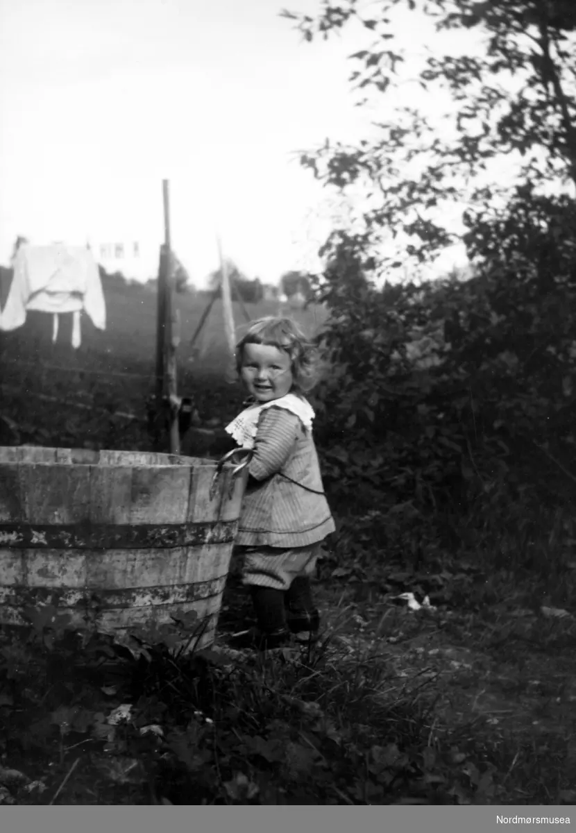 Et barn står ved en trestamp. Fra Nordmøre museums fotosamlinger.
