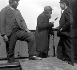 Foto av tre personer på et båtdekk. En ungdom, en middelaldr