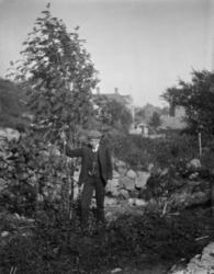 Foto av en ung mann, stående ved en steinmur. Muligens fra S