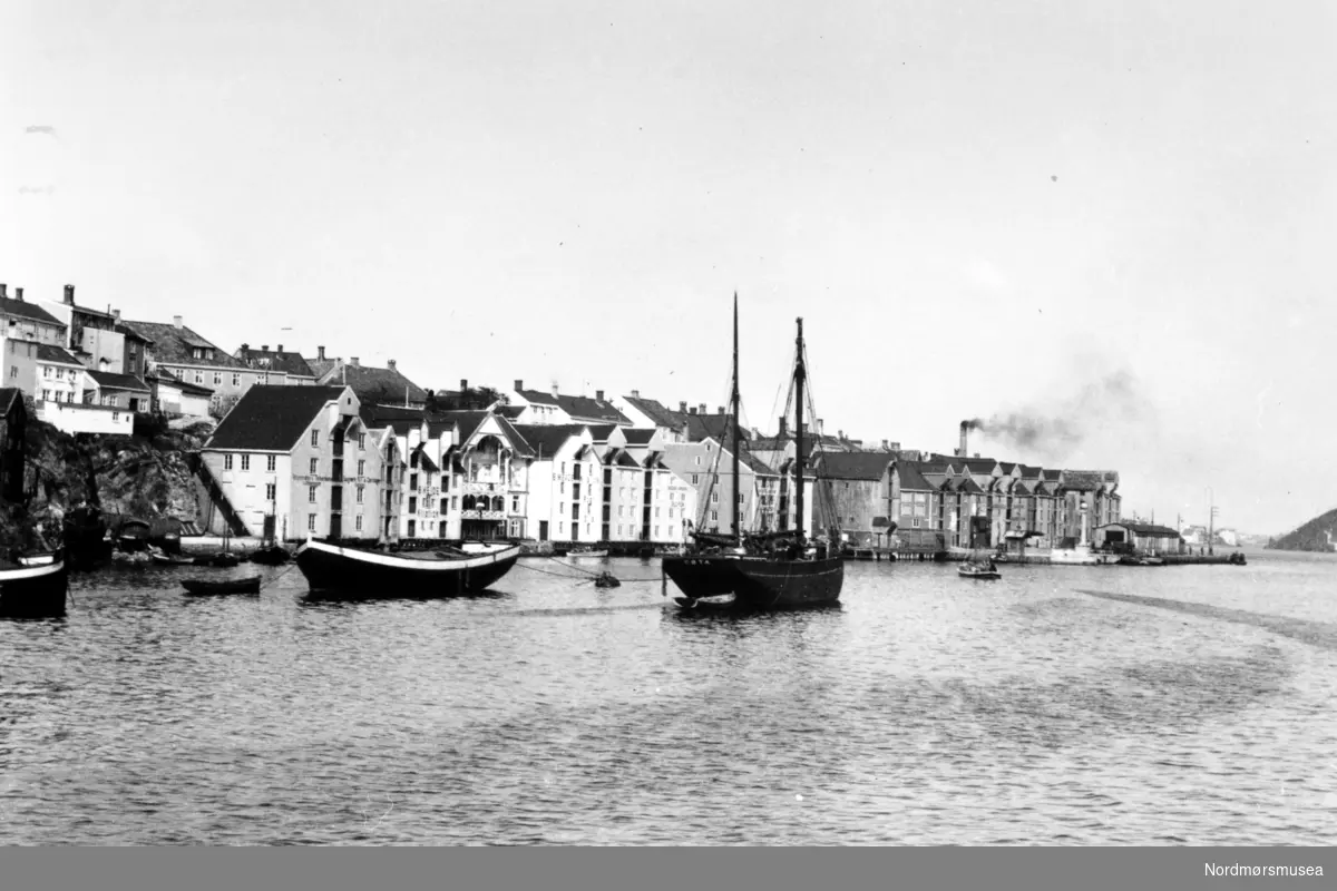 Foto fra Anders Beer Wilses fotoarkiv, hvor vi ser fra Sørsundet og Kirkelandet i Kristiansund. Her ser vi de gamle bryggene liggende på rad og rekke, og ute i Sørsundet ser vi blant annet en skonnert og en jekt. Fotoet er trolig fra perioden rundt 1910-1930. Fra Nordmøre Museums fotosamlinger.
