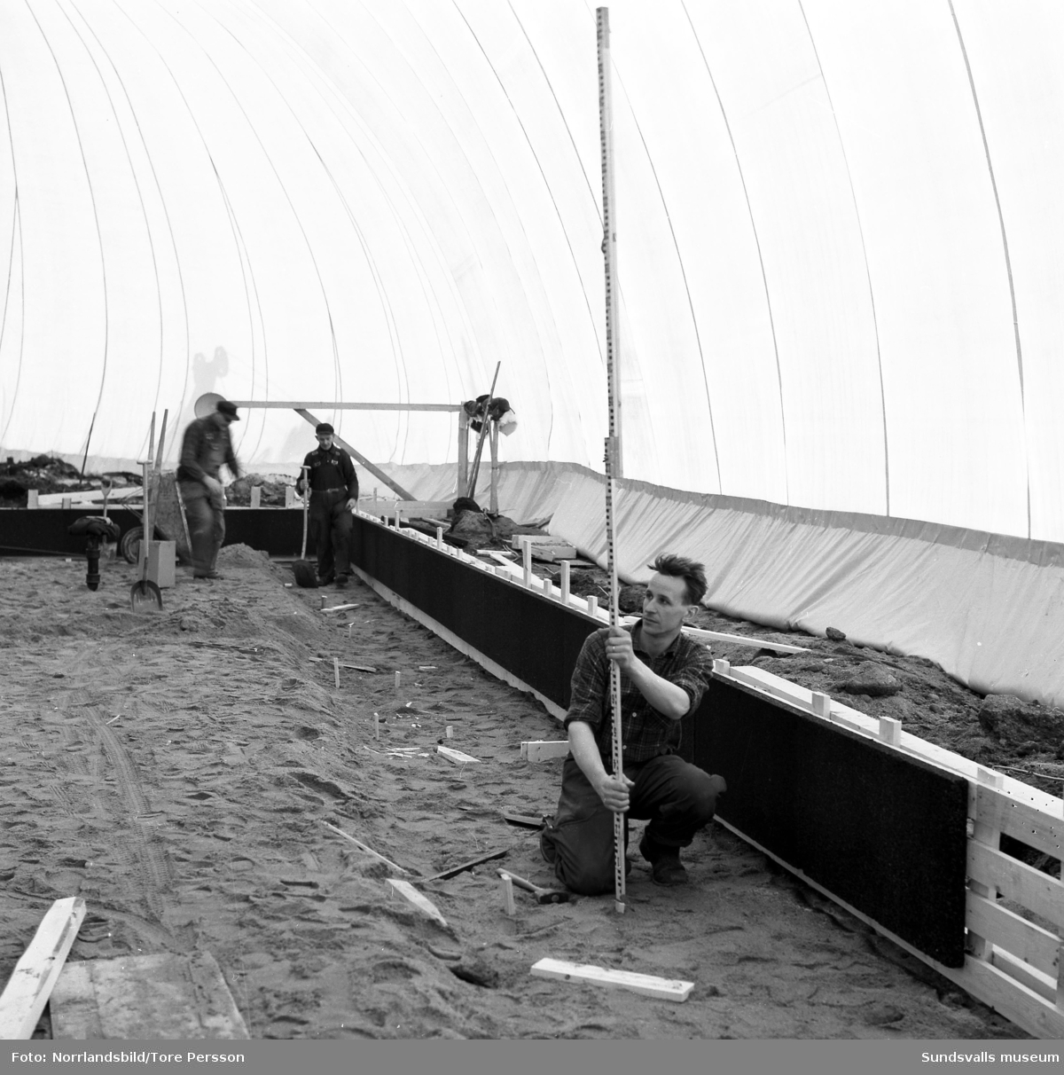 Husbygge i Granlo vid Vikingavägen-Höderbacken. Ett stort tält är uppställt och innanför tältväggarna pågår markarbetena för fullt.