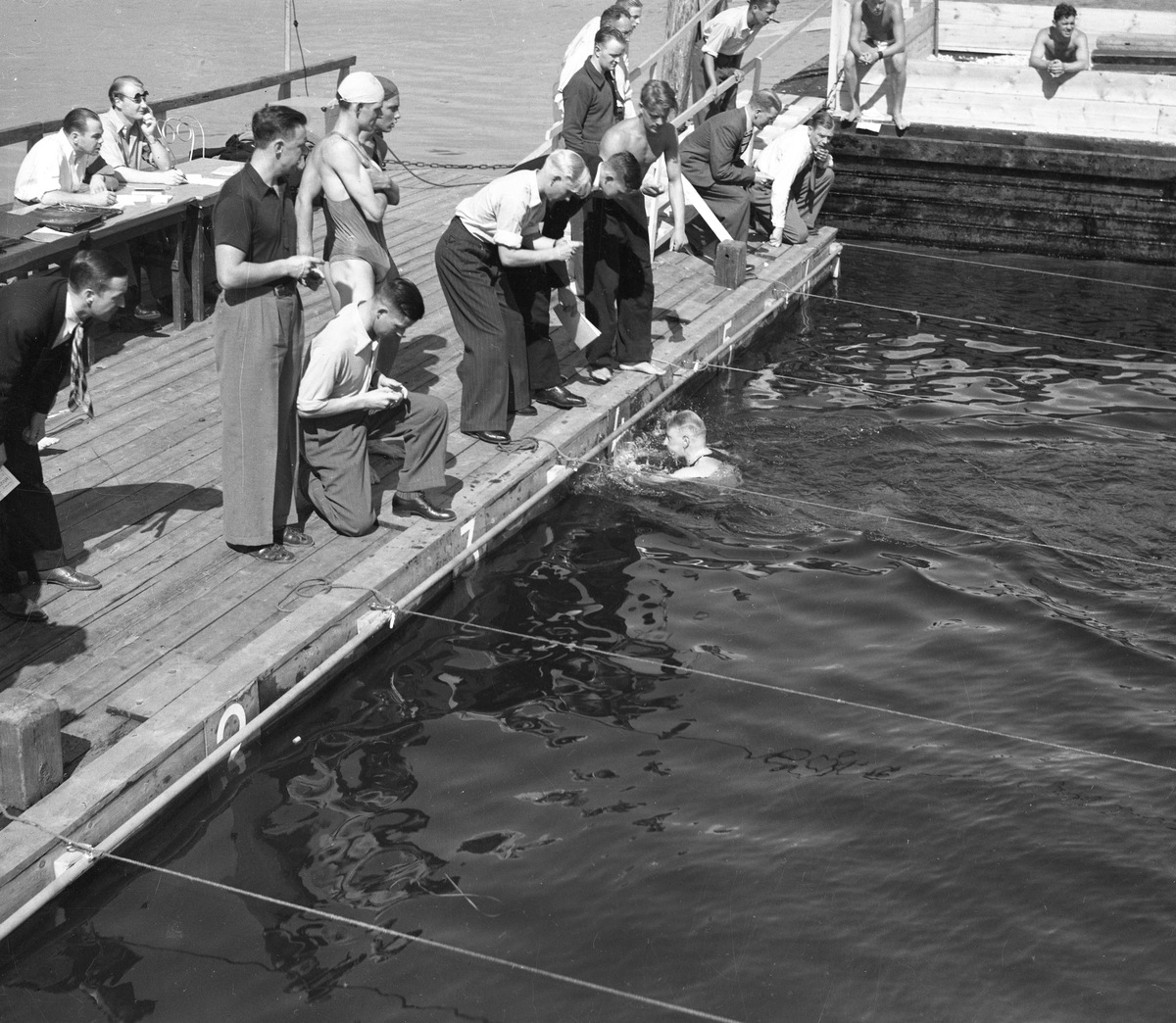 Bildserie från slutet av 1930-talet från Karlstads dåvarande simstadion. Anläggningen låg i anslutning till den s k badholmens östra sida söder om Kanikenäset. Badet invigdes 1923 och togs ur bruk och revs 1943 pga dålig vattenkvalité. En liknande konstruktion som ersatte den på bilderna byggdes upp i Örsholmstjärnet i början av 1950-talet.