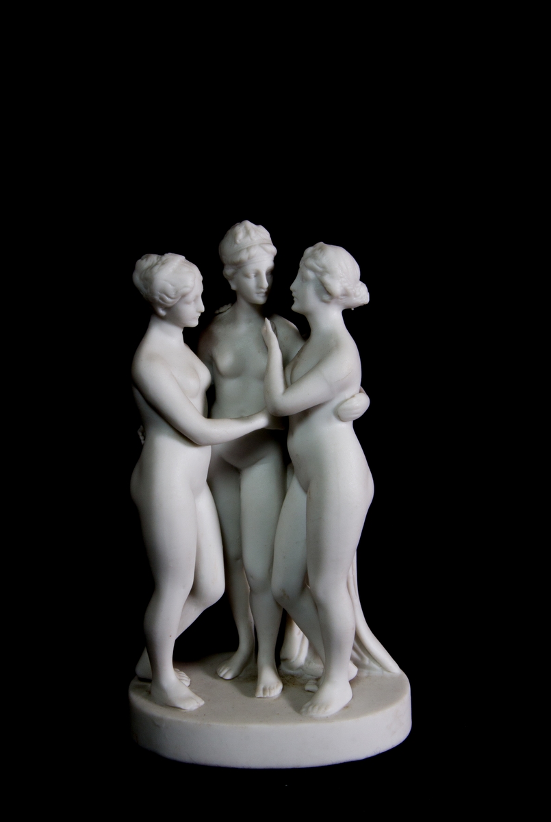 Studiemodell föreställande de tre gracerna i parian. De tre nakna kvinnorna i helfigur håller armarna om varandra. Bakom dem en draperad stubbe. Oval fotplatta.