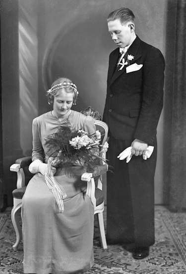 Foto av ett brudpar. Hon är klädd i färgad hellång brudklänning, med diadem i håret. Han bär smoking.
Helfigur. Ateljéfoto.
Trol. Torsten Verner Hagman (1915-1992), Rydaholm.
Källa: Sveriges Dödbok 1901-2009.