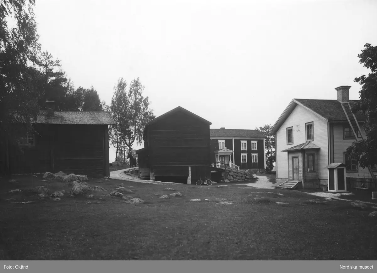 Bångagården (Bångsgården) i Runemo by, Alfta socken, Hälsingland. Gårdens byggnader samlade. En cykel står lutad mot ett av boningshusen. Mellan två byggnader skymtar en häst.