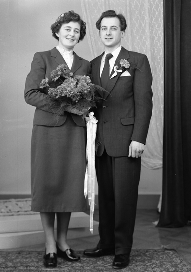 Foto av ett brudpar. Hon är klädd i dräkt och liten hatt. Han är klädd i mörk kostym och dito slips.
Helfigur. Ateljéfoto.
Gunnar Arvidsson f. 1929 i Moheda (1929-2013)
Alice Johansson f. 1934, Sköldstad Nybygget, Kvenneberga. 
Vigsel 9 april 1955.
