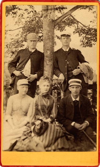 Grupporträtt av två kvinnor och tre unga män som grupperat sig runt ett träd. En av männen har studentmössa på sig, de övriga olika sommarmössor.