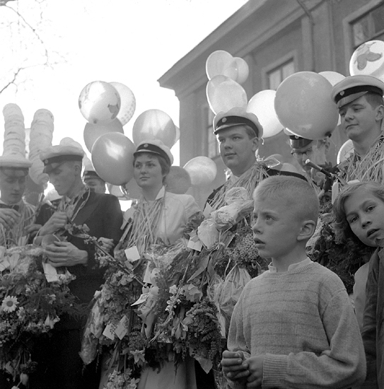 Studenterna, tredje d. 1960. 
Några studenter i väntan på talet vid Esaias Tegnérs 
staty. I bakgrunden skymtar det s.k. Karolinerhuset. 
(Motljusfoto).