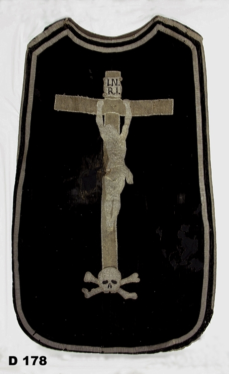 Mässhake av svart sammet, kantad med silvergaloner. På ryggsidan broderat krucifix i silver. Fodrad med grått linnetyg.
Daterad 1756.