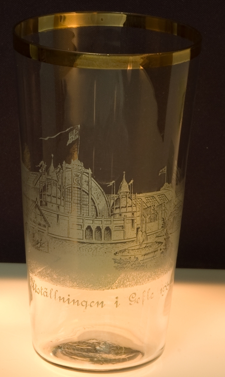 Dricksglas tillverkat för gefleutställningen 1901. Guldkant upptill. Maskinetsad dekot föreställande utställningens huvudentré och txt: Minnesutställningen i Gefle 1901.