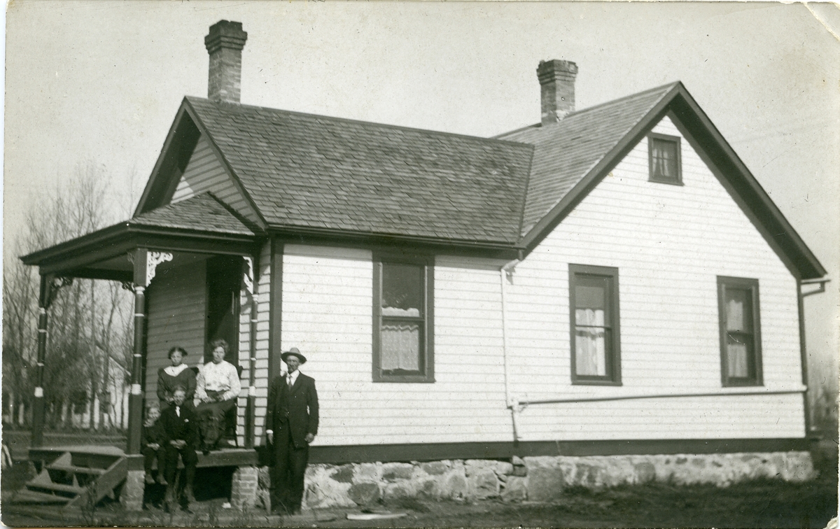 En familie avbildet på trappa utenfor farm-huset sitt.