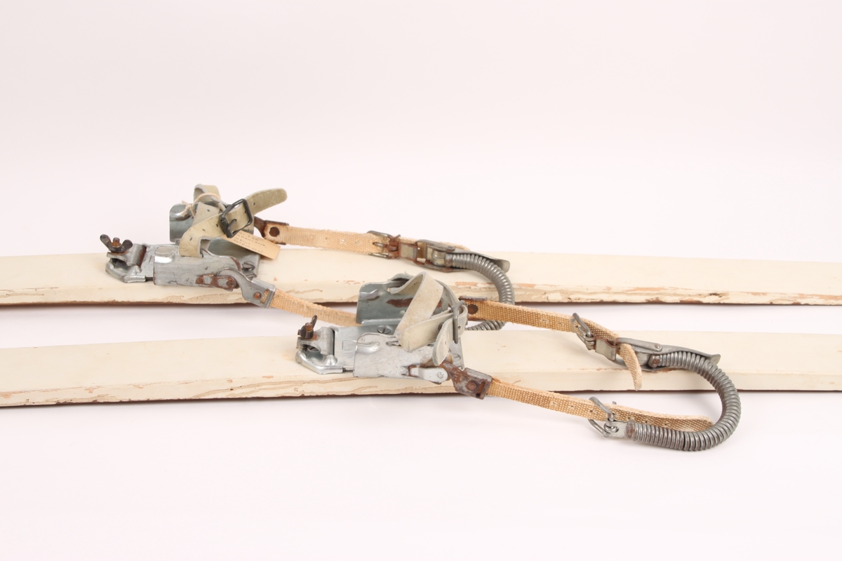 Et par hvitmalte treski med binding. Skiene har et metallbeslag på tuppen med hull. Skiene har også metallbeslag bak. Skiene har en rand under, samt lignokanter.