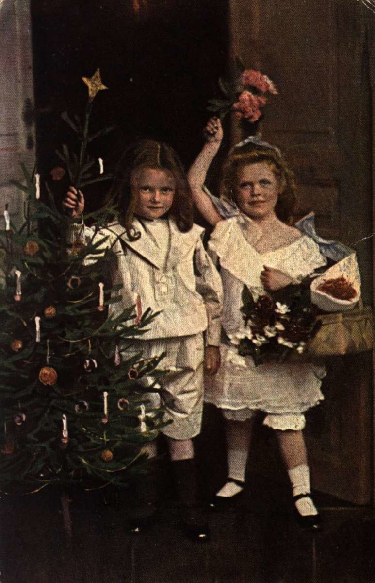 Julekort. Jule- og nyttårshilsen. Koloret fotografi. To piker ved et pynte juletreet. Stemplet 24.12.1918.