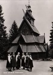 Postkort.Norsk Folkemuseum. Gol Stavkirke. Bunadkledd gruppe