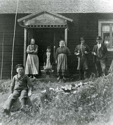Ett grupporträtt av troligtvis en familj stående framför ett hus med en förstukvist.