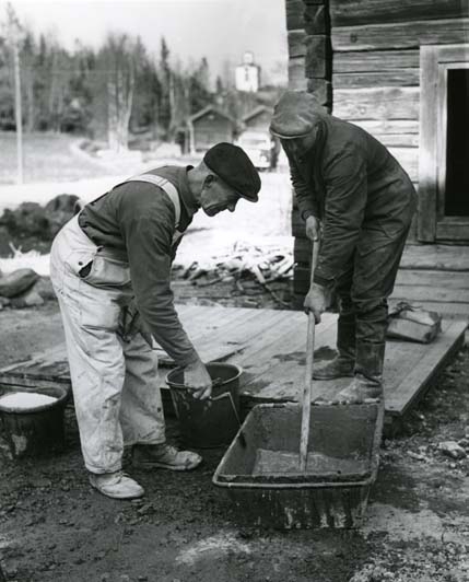 Två män blandar murbruk på en gårdsplan.