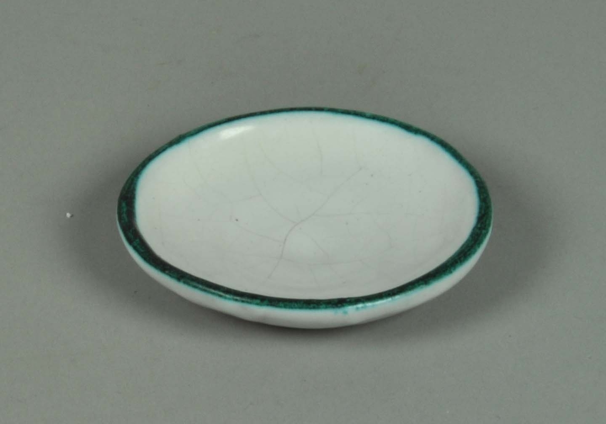 Keramikkskål med hvit glasur og påmalt grønn munningsrand.