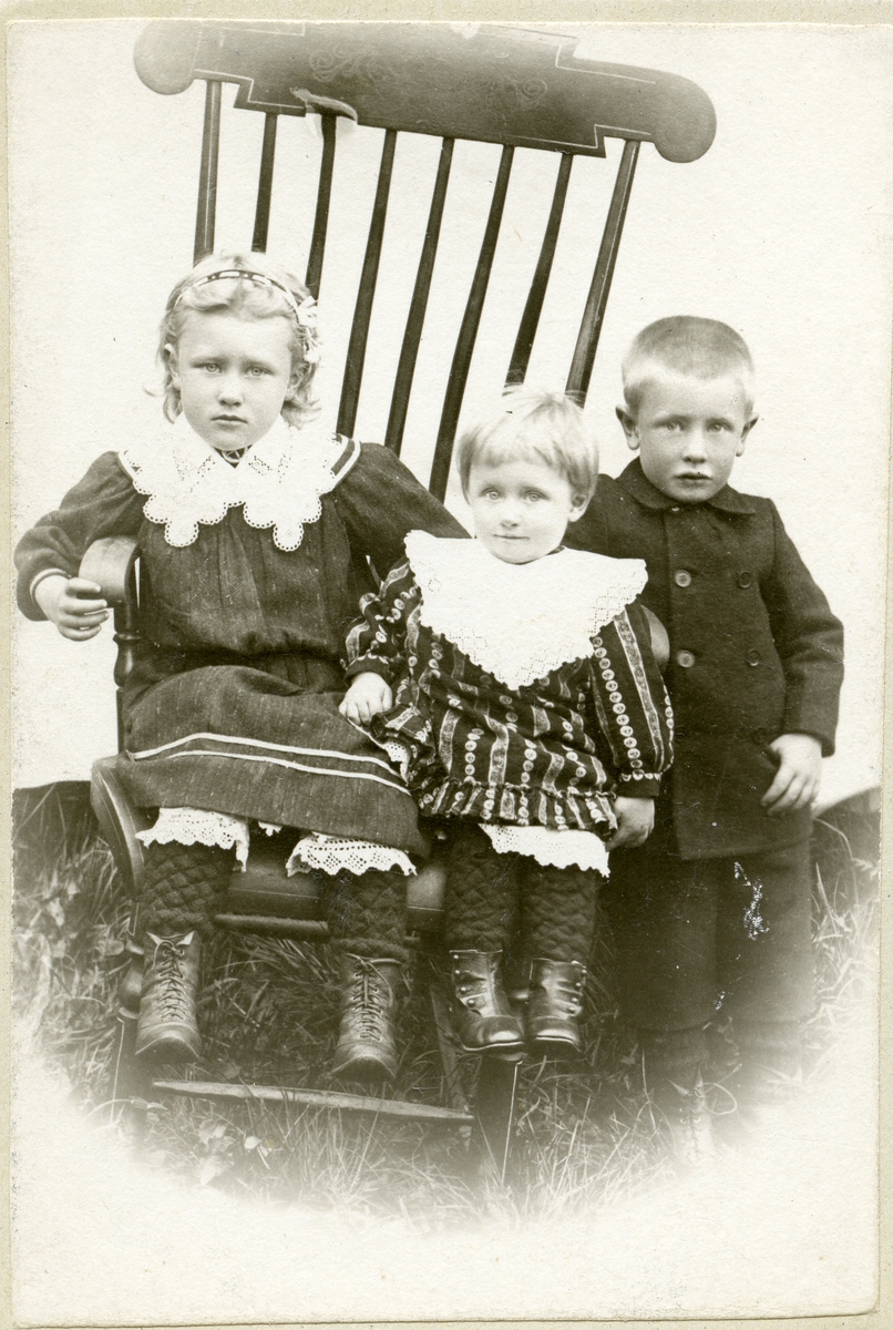 To jenter og ein gut sit i ein gyngestol. Truleg tatt 1910.