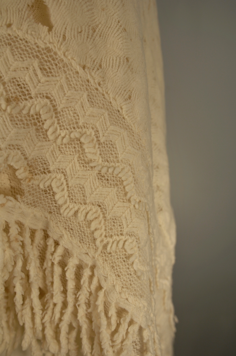 Strikket i tynn ulltråd. Den innerste firkanten er strikket i eit stykke. Knaten rundt påsydd slik at hjørnsne blir avrunda. Dersetter er det påsydd frynser med symaskin.