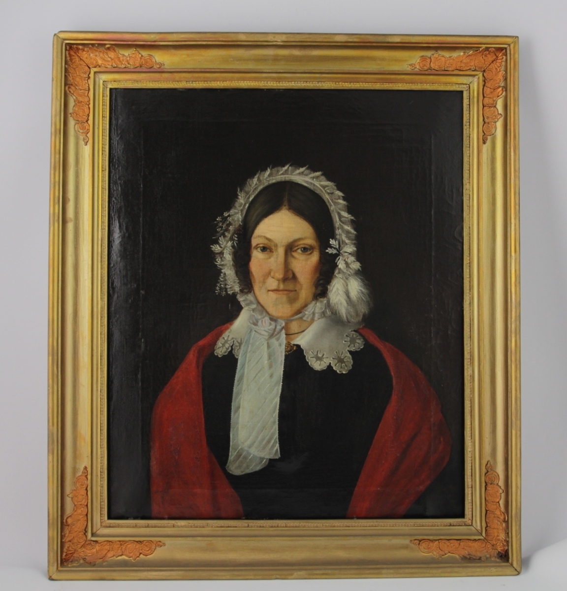 Halvportrett av en kvinne. Kvinnen bærer sort kjole med rødt sjal om skuldrene. Hette på hodet i hvitt, prydet med hvite fjær.