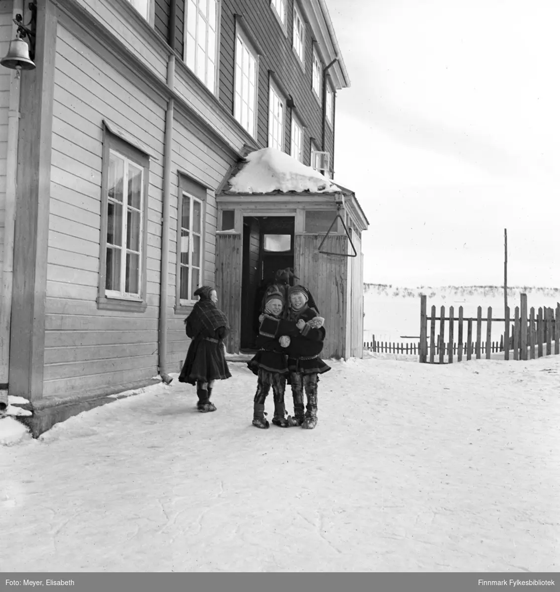 To skolegutter utenfor Kautokeino skoleinternat. Muligens en kvinnelig lærer til venstre i bildet. Skolen ble bygd i 1906. Påbygd i 1932 og ble brent i 1944.