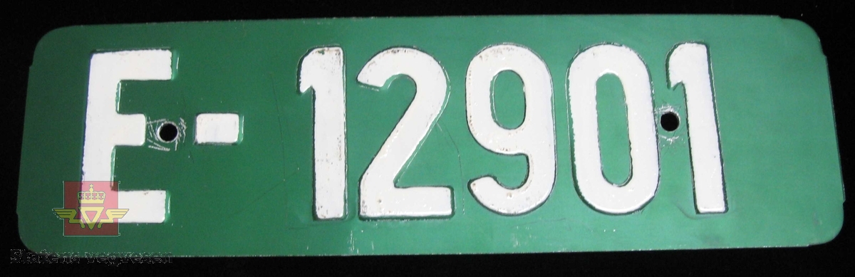Aluminium kjennemerke E- 12901. Hvit tekst i relieff på grønn bunn. Skiltet har to hull for fastsetting. 