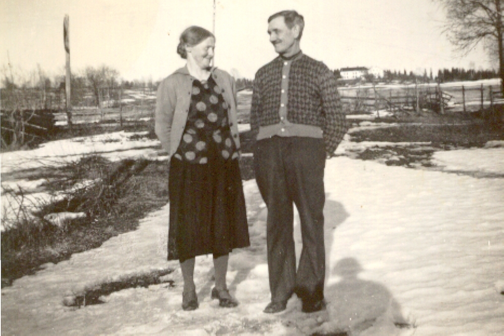 Karen Mathiasdatter Olsen (1883-1968) og Syver Olsen (1884-1957) i Verkenstua, Mengshoel. Husa på garden Mengshoel i bakgrunnen. Verkenstua ble revet i 1969.