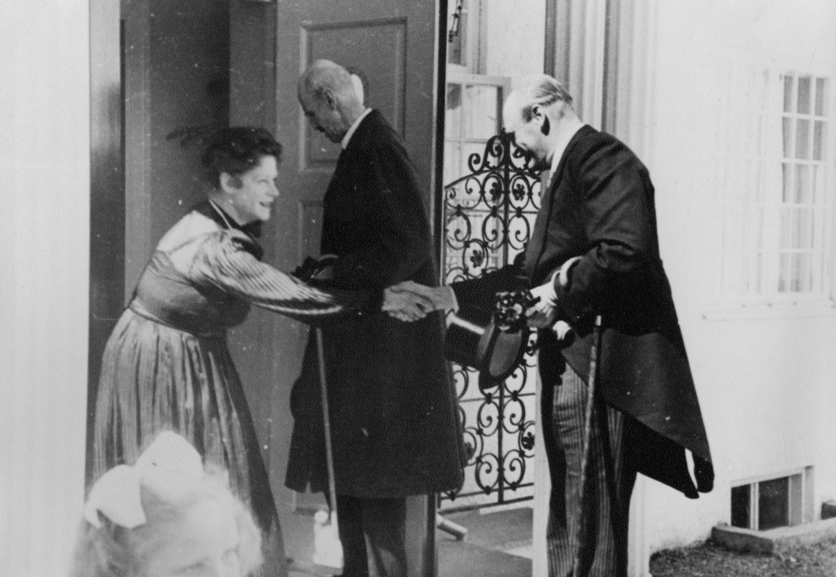 Victoria Bachke mottar kong Haakon VII og kronprins Olav som gjester til Ringve museum. Bildet er tatt på trappen til direktørboligen.