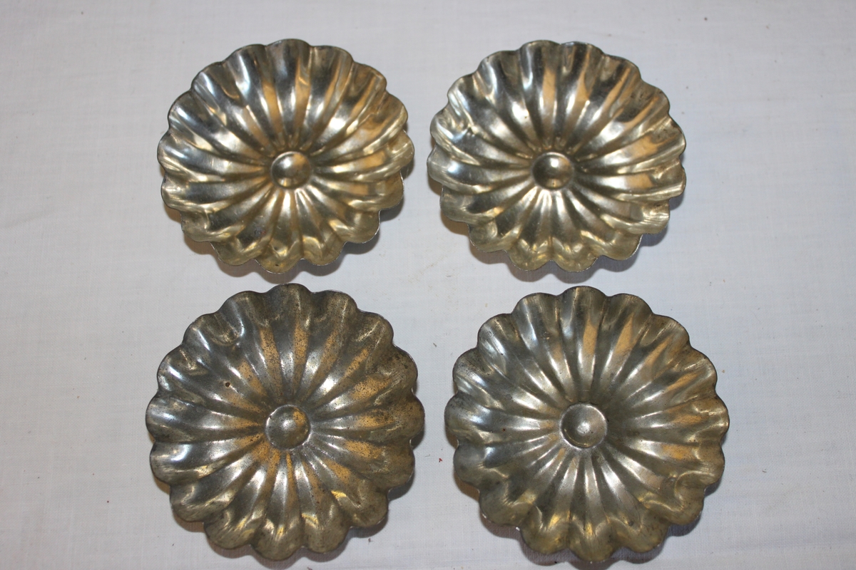 Fyra runda blomformade kakformar i plåt för mandelmusslor och liknande bakverk.