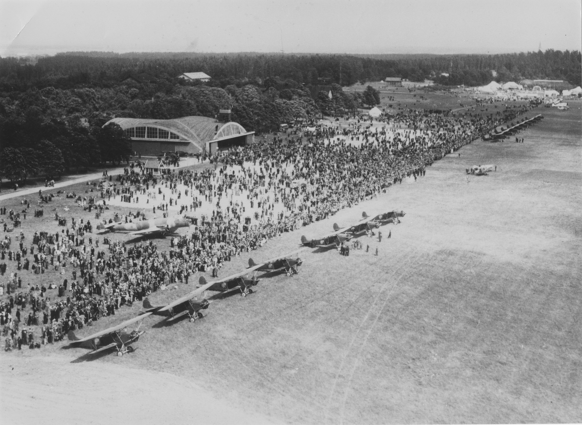 Flygdag på F 3 Malmen, 1930-tal. Flygfält fullt med besökare samt flygplan B 3 och S 6. I bakgrunden syns en hangar.