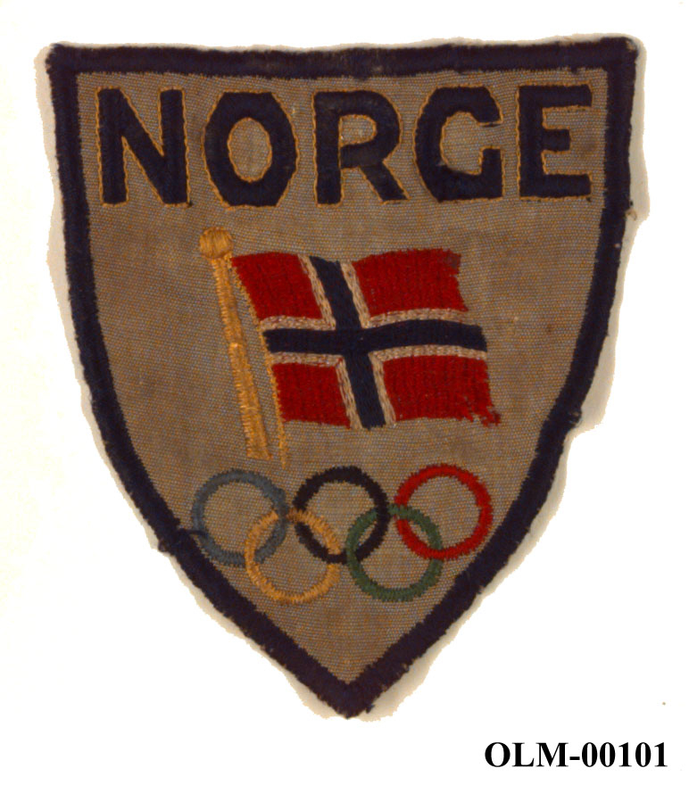 Brodert skjoldformet emblem til Norges Olympiske Komite, med norsk flagg og de olympiske ringer.
