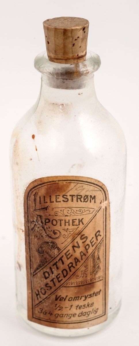 Rund glassflaske med korkpropp. Hvit dekorert etikett.