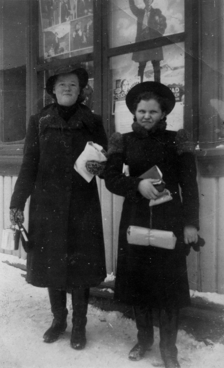 Ruth Kandola (t.h.) sammen med en annen ung dame, avbildet foran det som tilsynelatende må være en butikk. I vinduet bak ses diverse plakater.