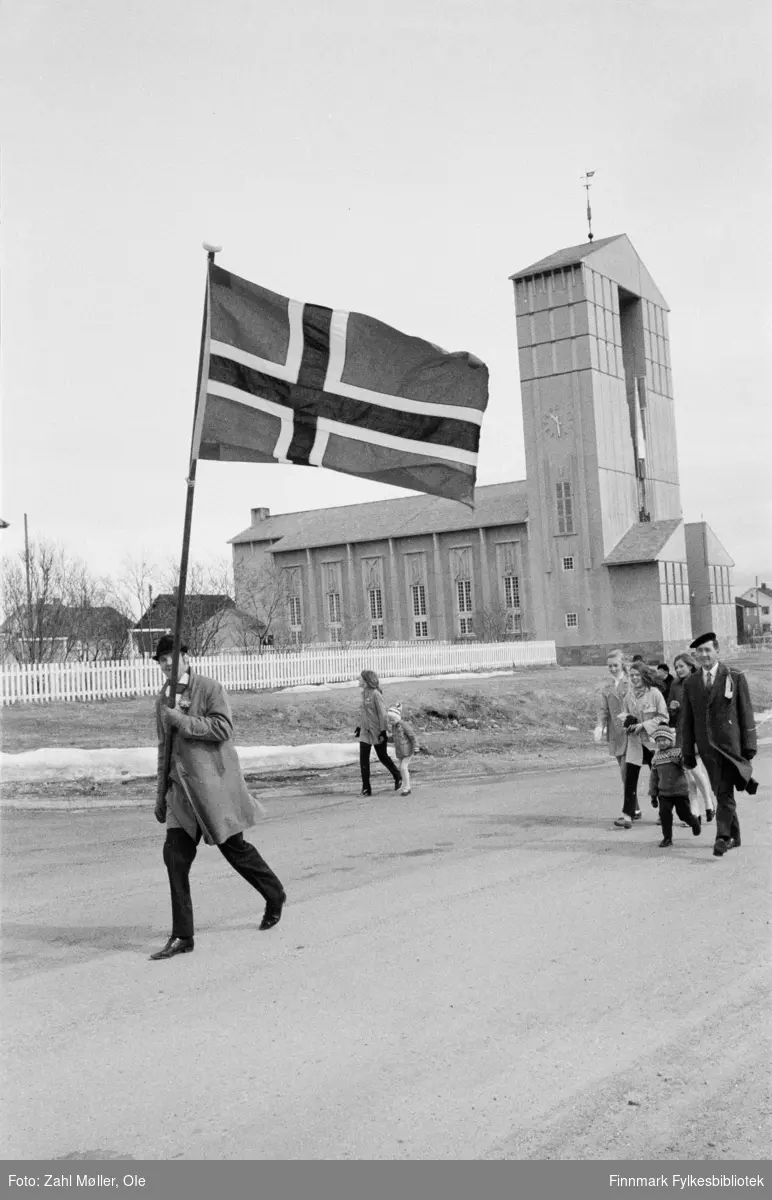 17.mai i Vadsø 1979. Fotografert av Ole Zahl Mölö. Fremst i toget går det en flaggbærer og toget har akkurat passert kirken.