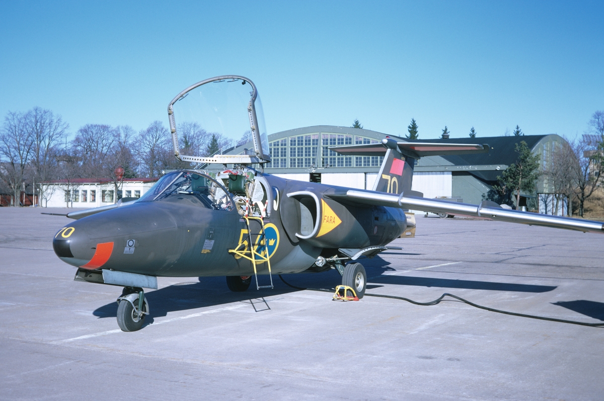 Flygplan SK 60 märkt nummer 70 ur F 5 Krigsflygskolan står på flygfältet på Malmen, 1973. Huven till förarhytten är uppfälld.