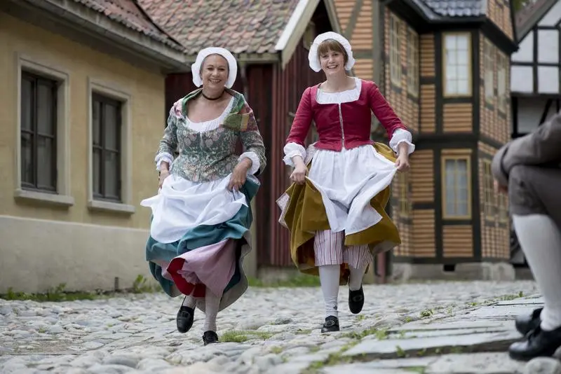 Two women in historical costumes walking on a cobblestone street in the Old Town at Norsk Folkemuseum.