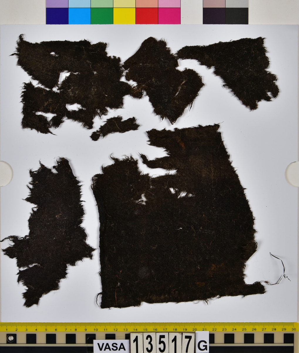Textil.
20 textilfragment uppdelade på fyndnummer 13517a-j.
Fnr 13517a består av två fragment av ull vävda i tuskaft. Det mindre fragmentet är trekantigt, har varit valkat på insidan och har fållar med sömmar kvar. Det stora fragmentet har två bevarade originalkanter.
Fnr 13517b består av två fragment av ull vävda i 2/1-kypert.
Fnr 13517c består av två fragment av ull vävda i tuskaft. Det större fragmentet har ett hål i mitten. De är svarta av tjära och har troligen varit en del av en becksudd.
Fnr 13517d består av ett fragment av ull vävt i 2/1-kypert.
Fnr 13517e består av ett fragment av ull vävt i 2/2-kypert.
Fnr 13517f består av ett fragment av ull vävt i tuskaft.
Fnr 13517g består av 6 fragment av ull vävda i tuskaft. Två av fragmenten ser ut att ha varit valkade på ena sidan. Tre av fragmenten har vissa originalkanter eller -fållar kvar.
Fnr 13517h består av ett fragment av ull vävt i tuskaft.
Fnr 13517i består av 3 fragment av ull vävda i tuskaft. Fragmenten kan ha varit valkade på ena sidan. Ett fragment är ljusare i färgen än de andra.
Fnr 13517j består av ett filtat fragment av ull eller bäver. I en av kanterna finns hål efter en söm.






TEXTILDOKUMENTATION 2018:

Fyndnummer: 13517c
Kontextgrupp: HS5
Typnummer: HS5.1:1 (till höger i bild)

Fragment i tuskaftsvävd ull och ruggad/valkad med en mycket tät lugg. Fragmentet är rektangulärt, har uppfransade kanter och ett spikhål i mitten (3-4 mm). I mitten på ena sidan finns ett vagt fyrkantigt avtryck (28 x 25 mm) och på andra sidan ett ovalt avtryck (35x47 mm). Dessa avtryck är troligtvis efter en fyrkantig läderbit och ett runt skaft vilket talar för att detta fragment har tillhört en becksudd. Tyget har veckats och brustit mot avtrycket. Fragmentet har synliga rester av tjära/beck samt bastfiber som ligger ovanpå. Fragmentet är relativt mjukt.

TEKNIK
Trådsystem 1
Trådtäthet (tr/cm): 8
Garn nr: 1
Fibermaterial: ull
Garngrovlek (mm): 0,77-1,01 
Antal trådar: 1
Spinnriktning: Z
Spinnvinkel (grader): 15,79-29,62 
Färg: mörkbrun originalfärg okänd

Trådsystem 2
Trådtäthet (tr/cm): 8
Garn nr: 2
Fibermaterial: ull
Garngrovlek (mm): 0,67-0,87 
Antal trådar: 1
Spinnriktning: S
Spinnvinkel (grader): 14,19-30,56 
Färg: mörkbrun originalfärg okänd




Fyndnummer: 13517c
Kontextgrupp: HS5
Typnummer: HS5.2:1 (till vänster i bild)

Fragment i ull, vävt i 2/2 kypert och tuskaft (4 skaft). Fragmentet har vridit och vikt sig så att de z-spunna respektive de s-spunna trådarna ser ut att tillhöra olika trådsystem. Detta är på grund av vridningen och i själva verket är det en fram- och en baksida man ser. Stora mängder långa bastfibrer sitter invirade i fragmentet, liksom en sten. På fragmentet finns även rester av vad som kan vara tjära eller beck.
I mikroskop har fibrerna en jämn, tydlig och intensiv svart färg. Att fibrerna är så pass jämna i färgen kan tyda på att de är färgade.

TEKNIK
Trådsystem 1
Trådtäthet (tr/cm): 9-10
Garn nr: 1
Fibermaterial: ull
Garngrovlek (mm): 0,61-1,01 
Antal trådar: 1
Spinnriktning: Z
Spinnvinkel (grader): 34,25-40,51 
Färg: svart

Trådsystem 2
Trådtäthet (tr/cm): 9-10
Garn nr: 2
Fibermaterial: ull
Garngrovlek (mm): 0,69-1,06
Antal trådar: 1
Spinnriktning: S
Spinnvinkel (grader): 21,78-28,09
Färg: svart